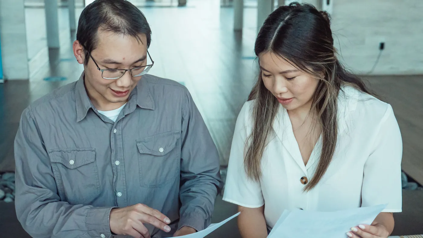 Two colleagues in an office reading through printed documents together