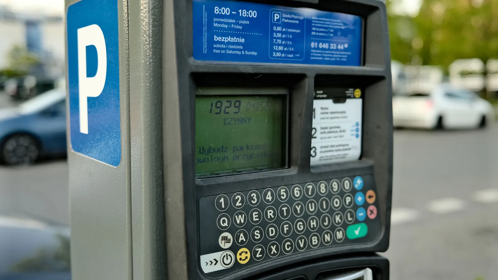 A digital parking meter on a city street with cars passing behind it
