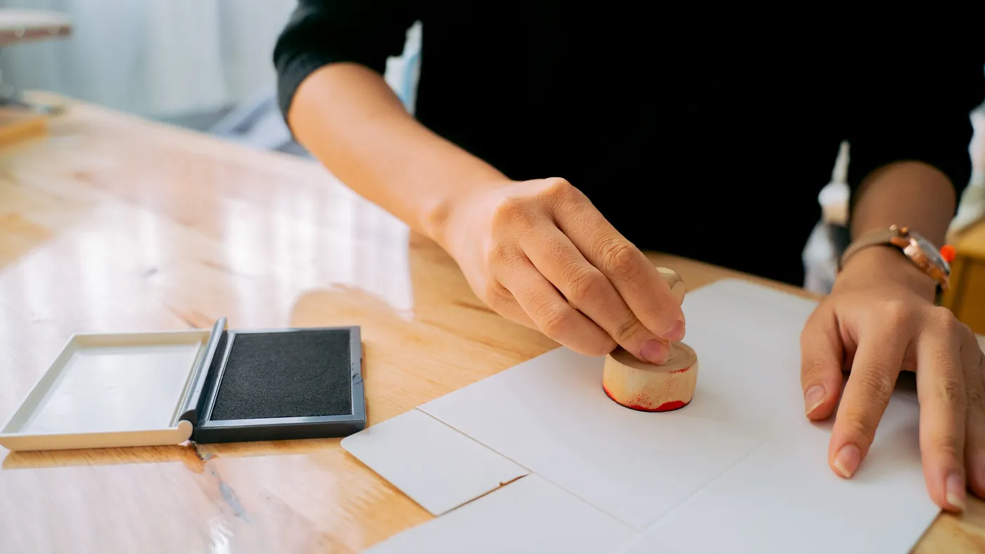A person's hand pressing a rubber stamp onto a paper document on a wooden desk