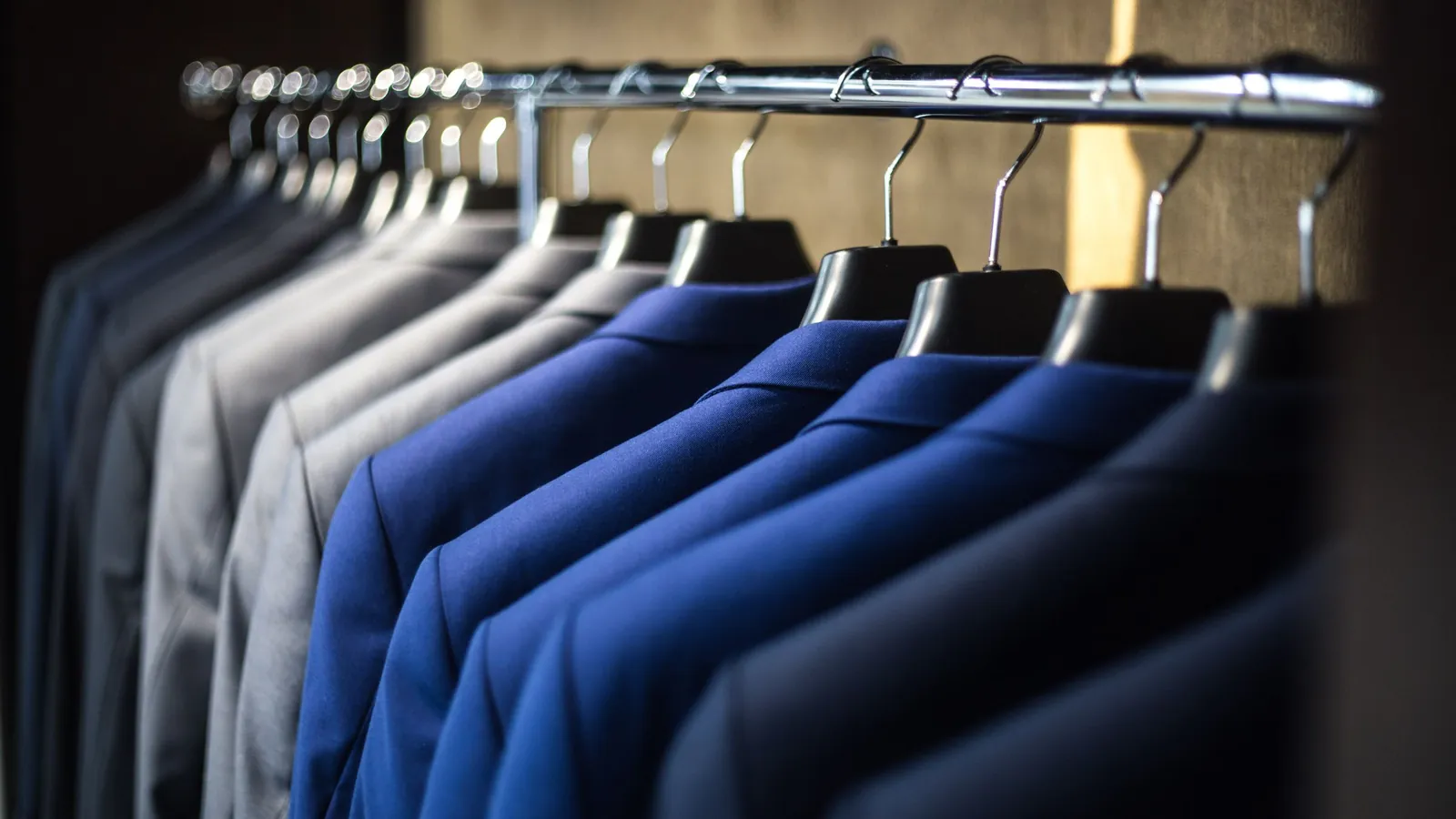 A row of blue and grey suit jackets hanging on black hangers along a shop rail