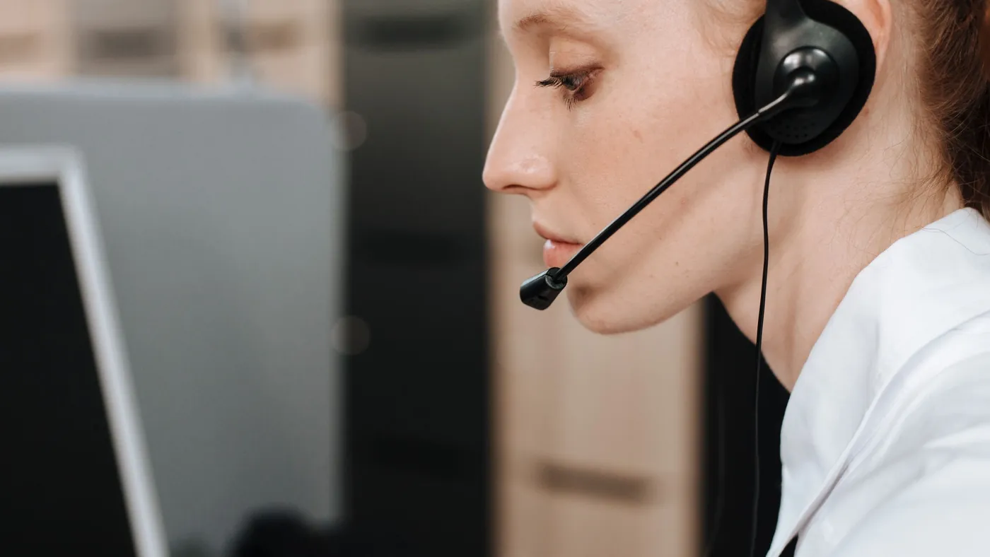 A customer support representative wearing a headset works at a desk in an office