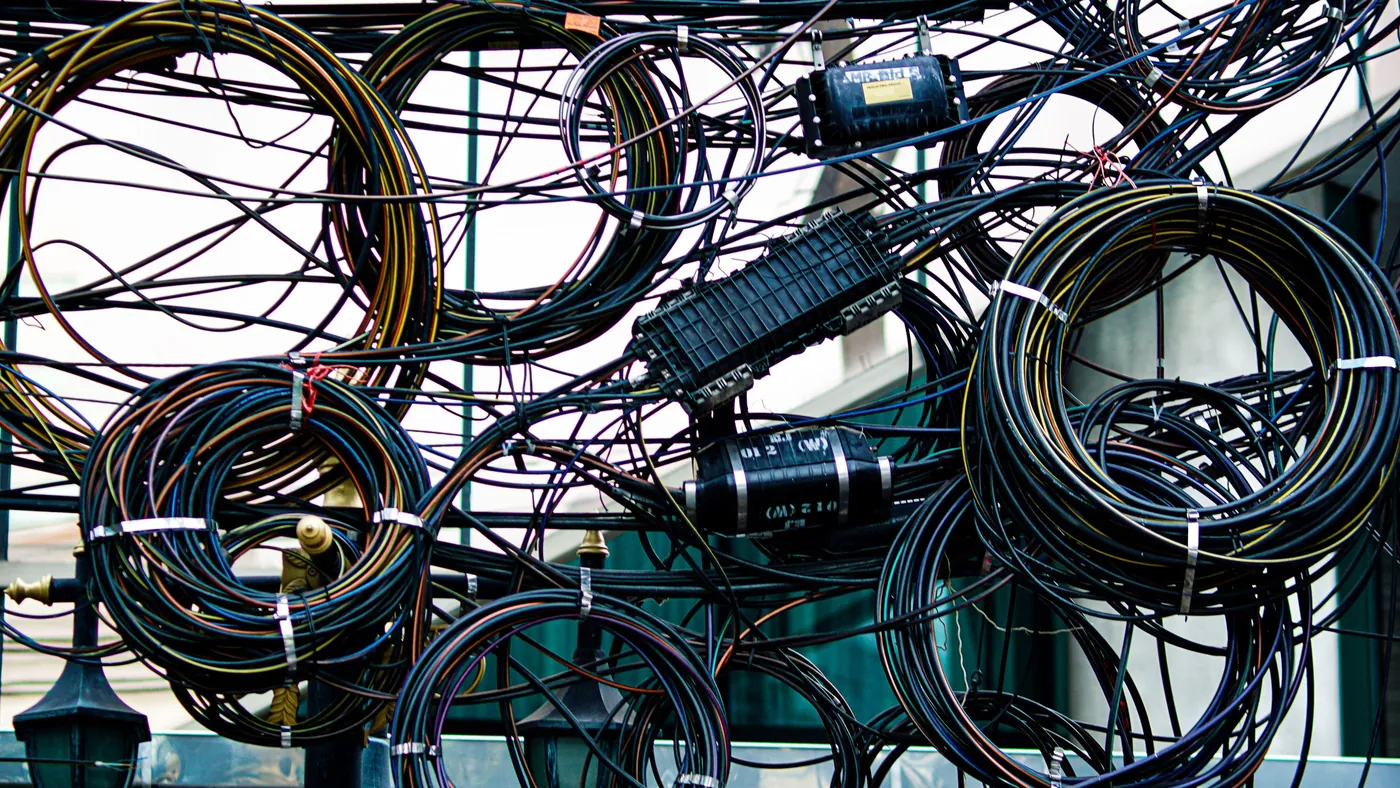 A dense tangle of power and communication cables knotted together outdoors