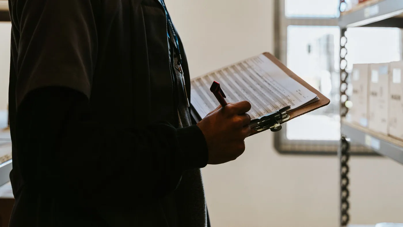 A worker in a warehouse holding a clipboard and marking off a printed checklist