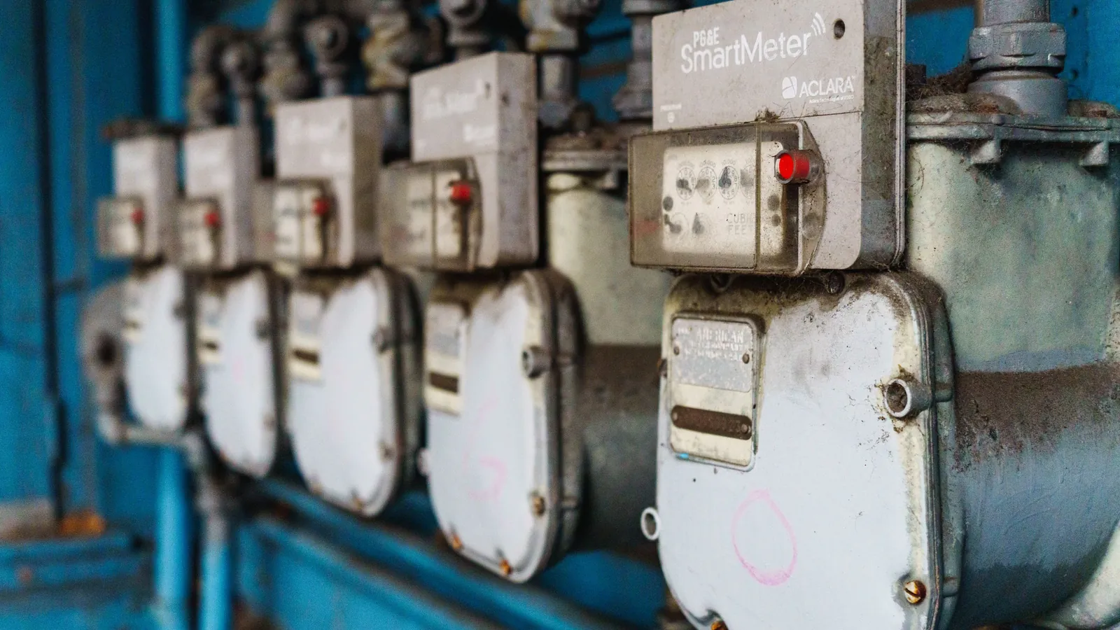A row of industrial utility meters mounted on a blue wall