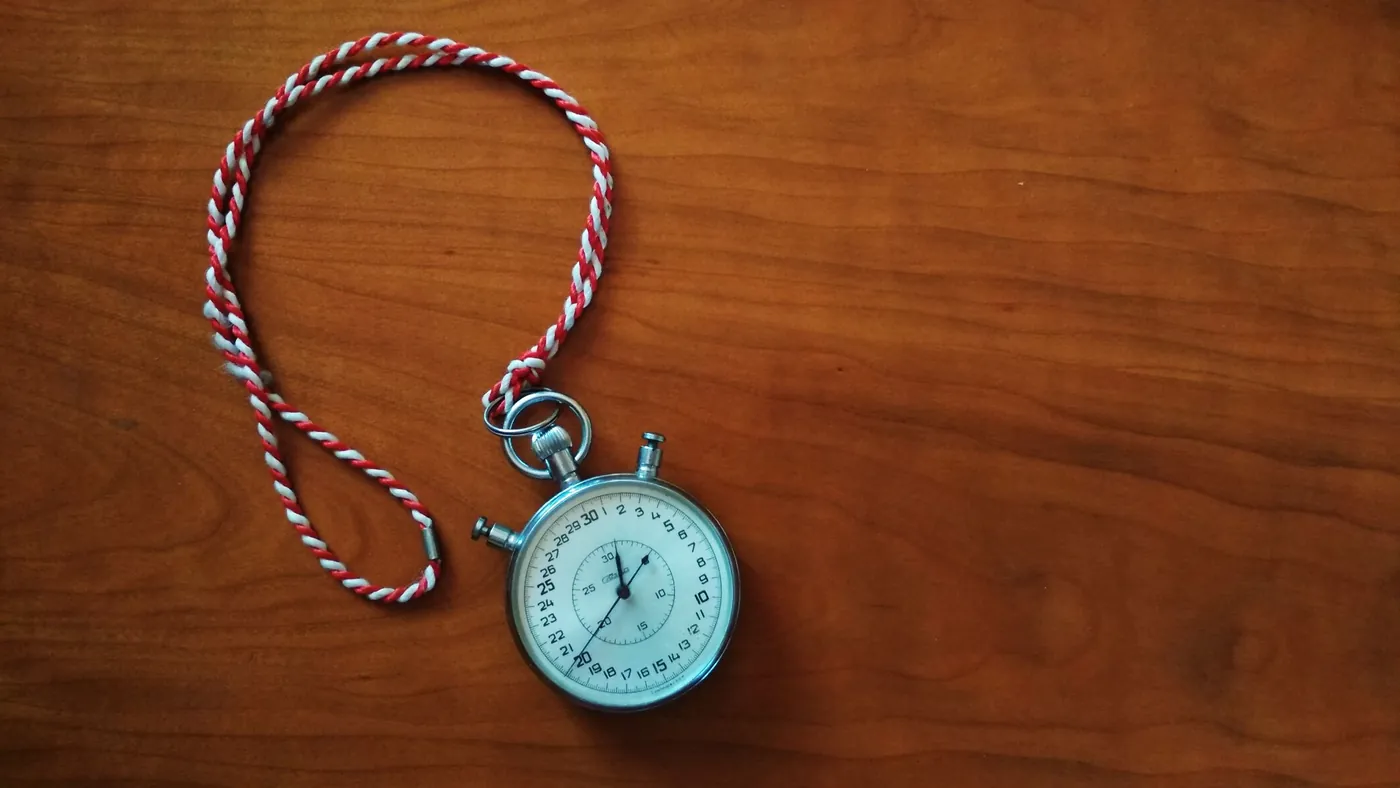 An antique silver stopwatch on a red and white cord lying on a wooden table