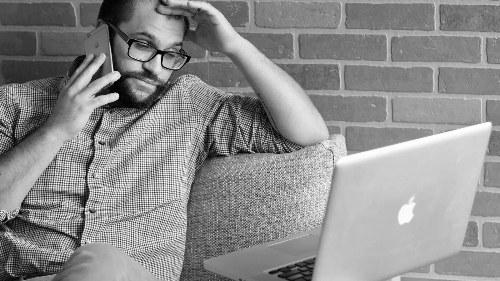 A man on a phone call rubbing his forehead while looking at a laptop