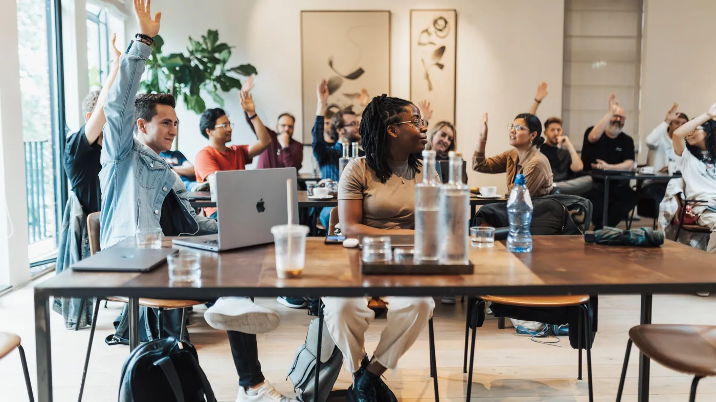 A group of adults with hands raised during a workshop session indoors