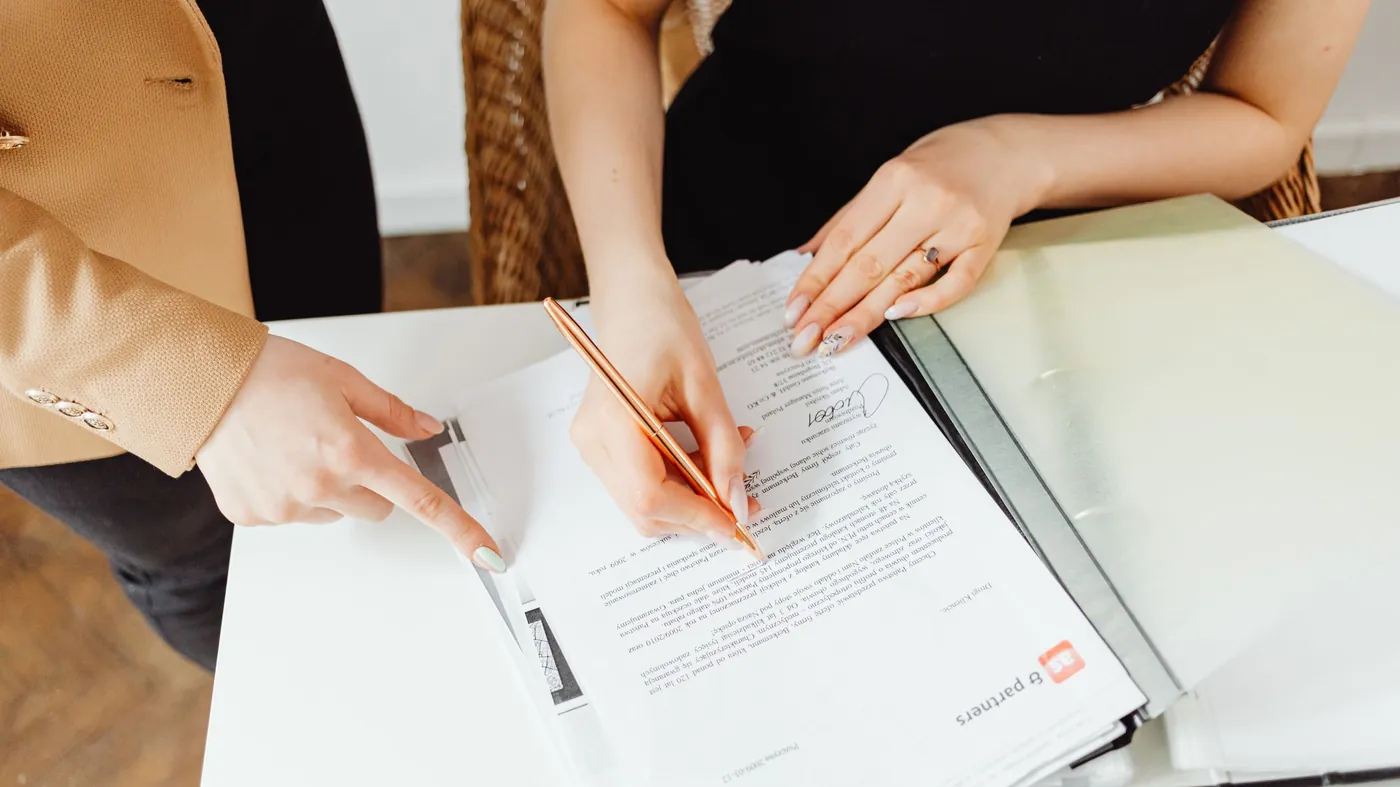 Two people at an office desk signing paperwork with a pen