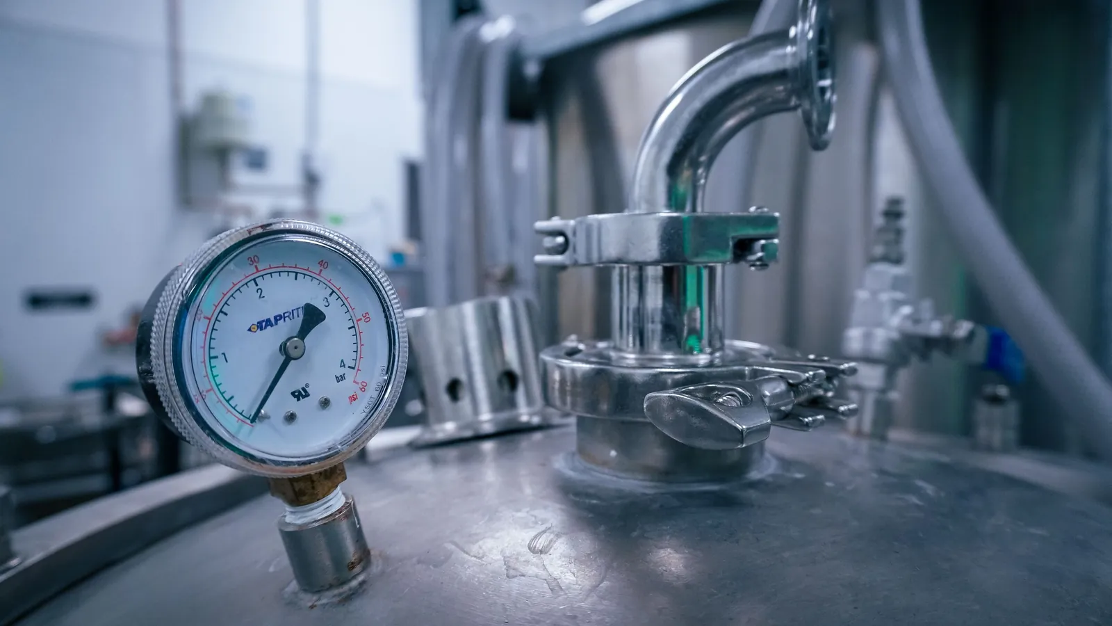 An industrial pressure gauge mounted on a stainless steel tank beside a valve