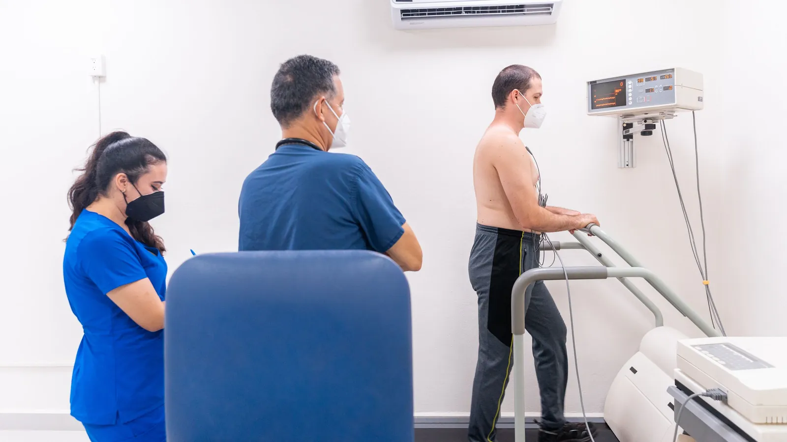 A cardiologist watching monitors while a patient walks a treadmill during a cardiac stress test