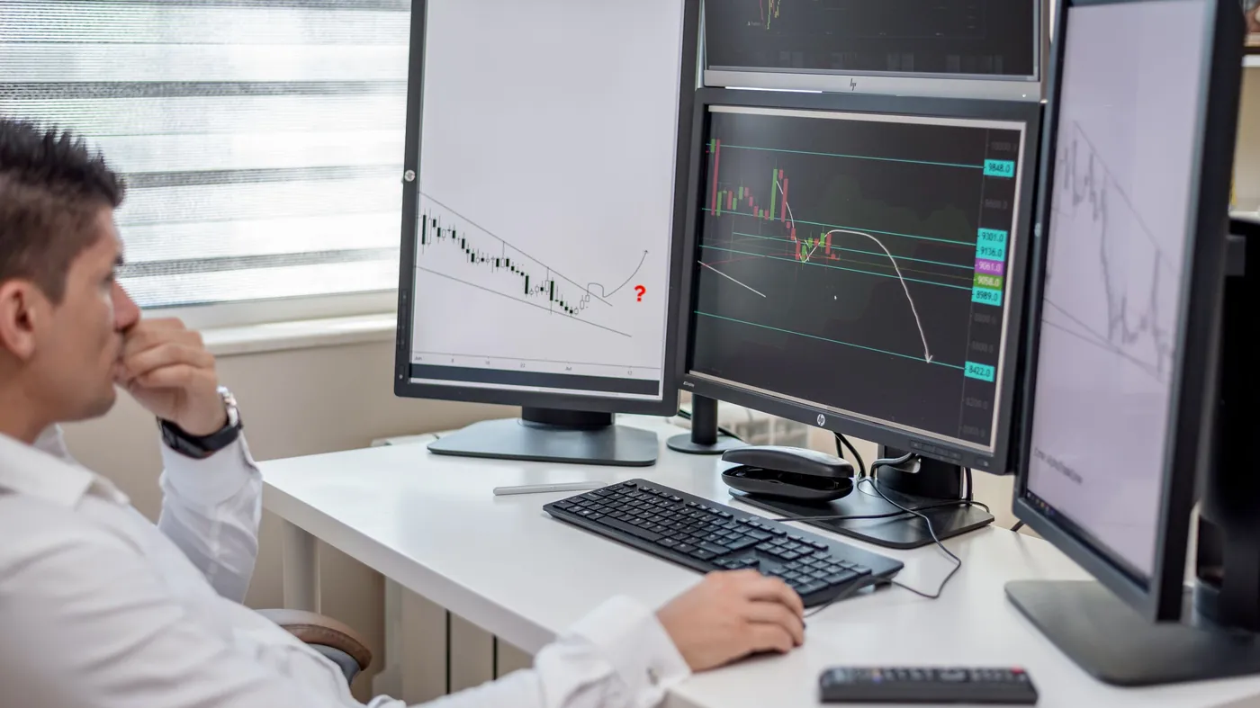 A business professional reviewing data across several computer monitors at a desk