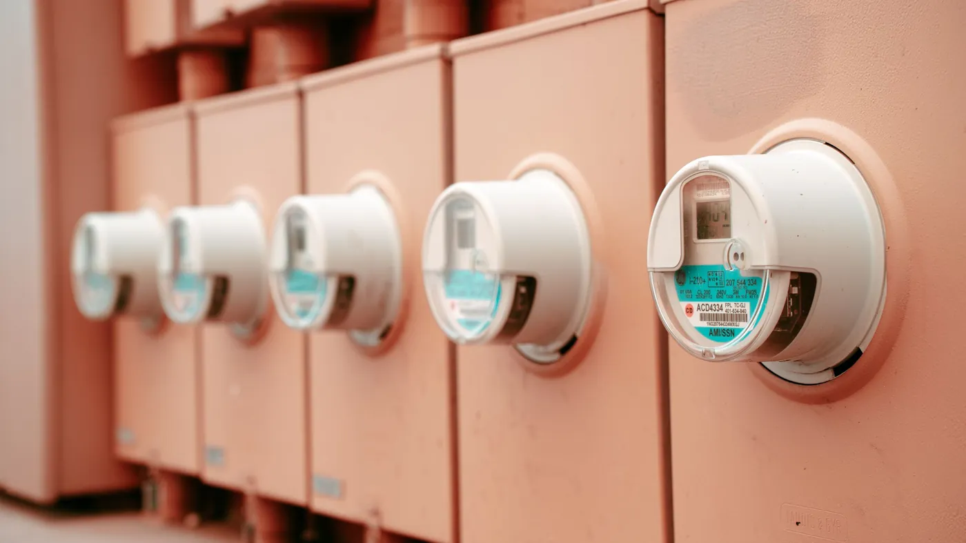 A row of electricity meters in pale enclosures mounted side by side on an industrial wall