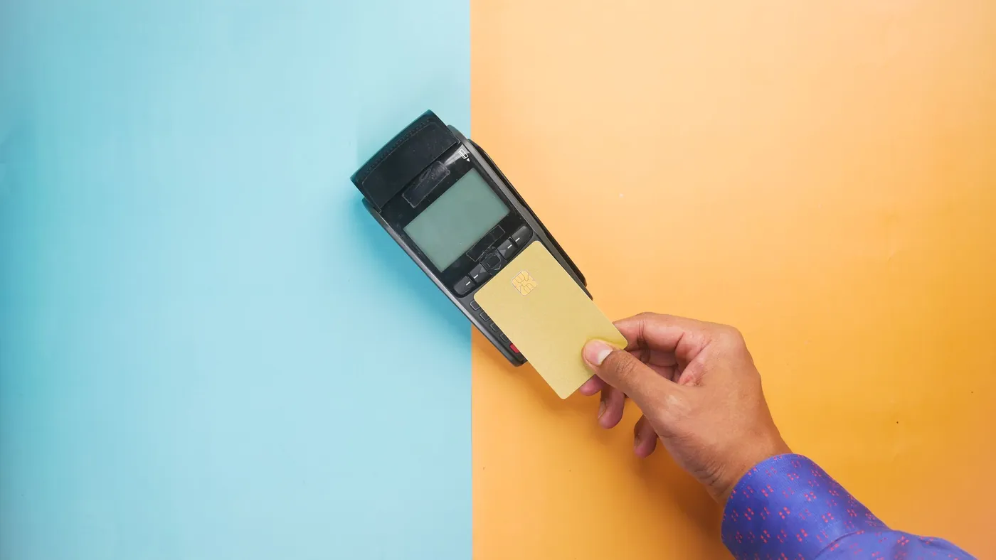 A hand holding a payment card against a card terminal on a split blue and orange background