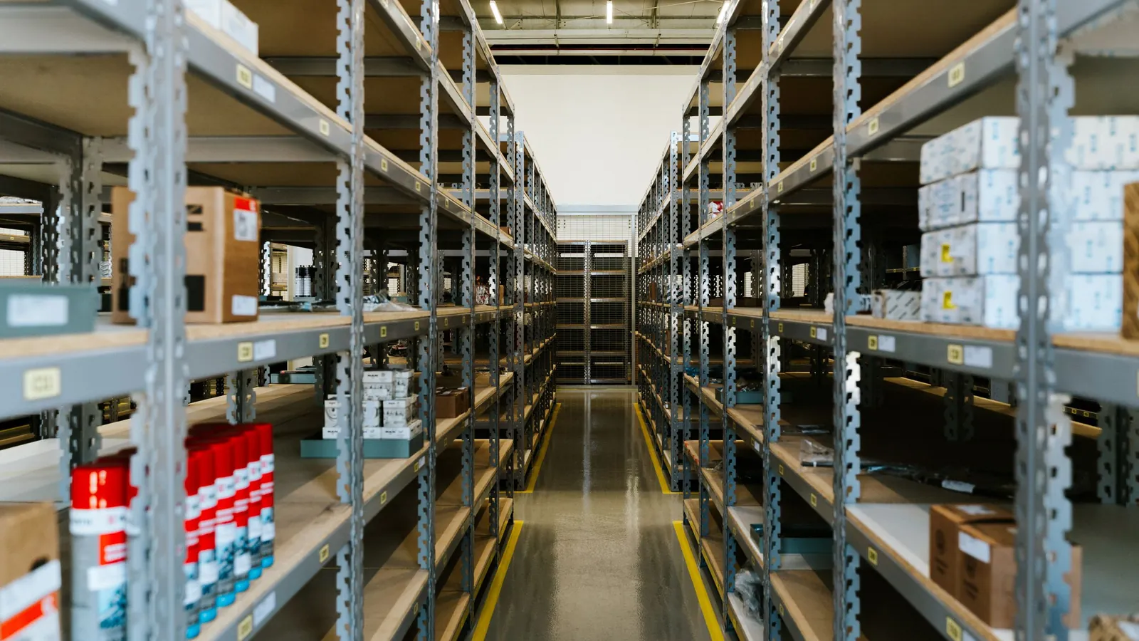 A narrow walkway between tall metal warehouse shelves stacked with stored merchandise
