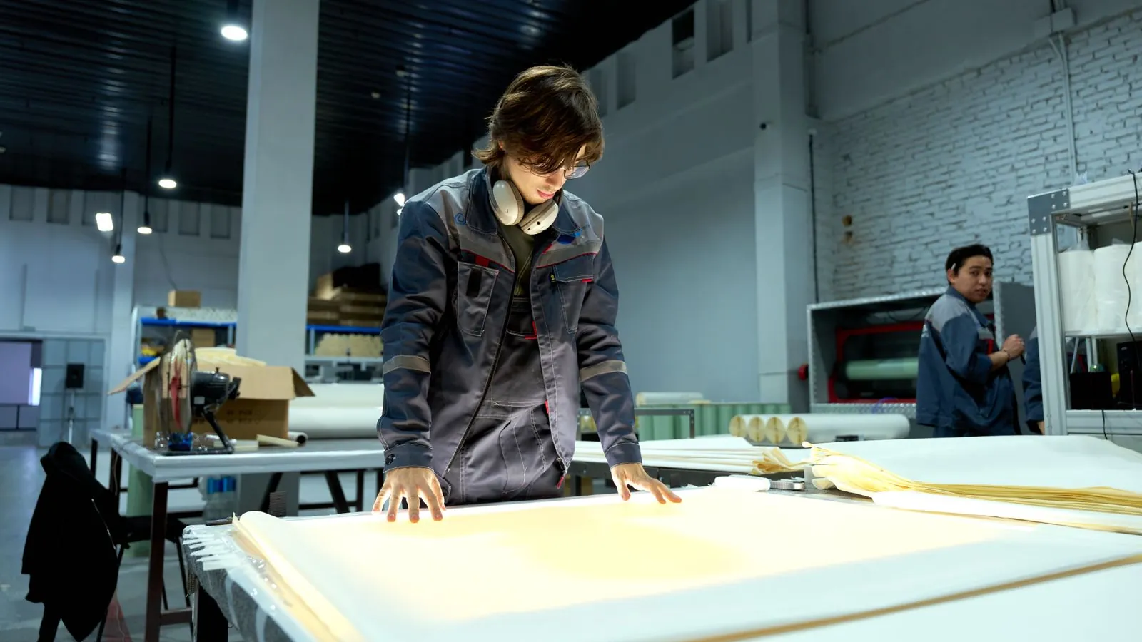 A worker inspecting sheets under bright light in a factory