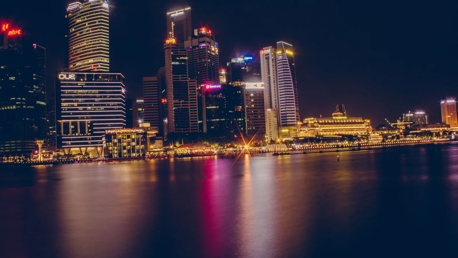 The Singapore waterfront at night, with lit office towers reflected in the bay