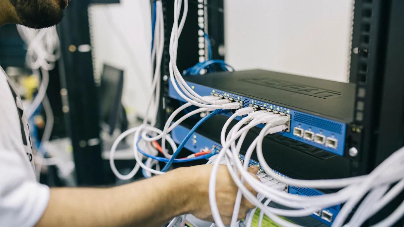 An engineer connecting network cables at the back of a server rack