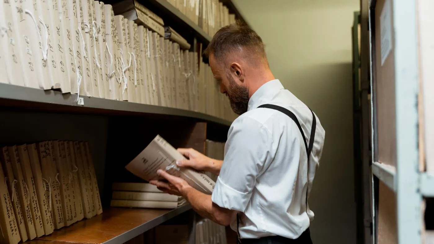 A man pulling a file from a shelf of stored documents in an archive room