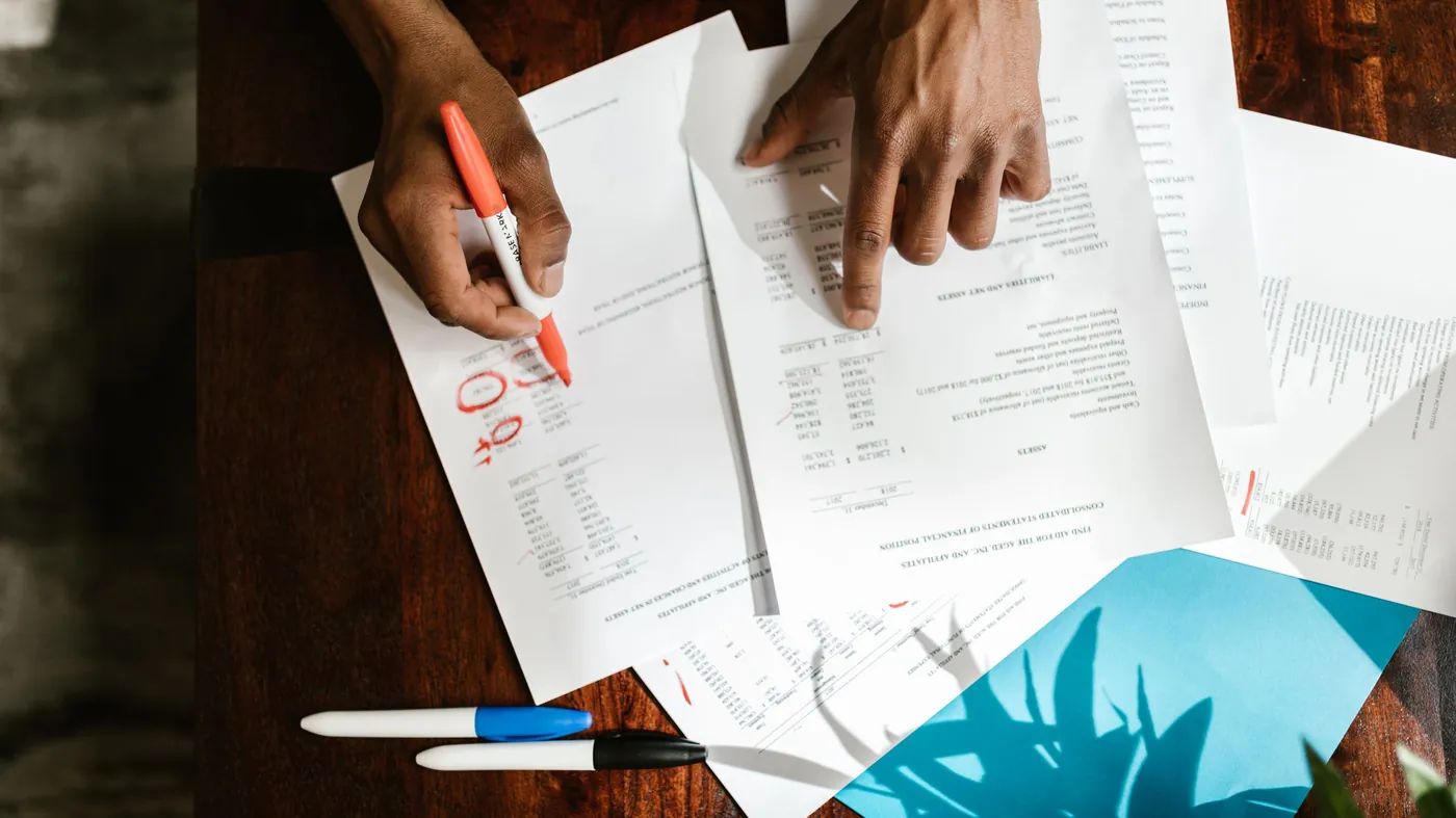 Overhead view of hands marking up printed financial documents on a desk
