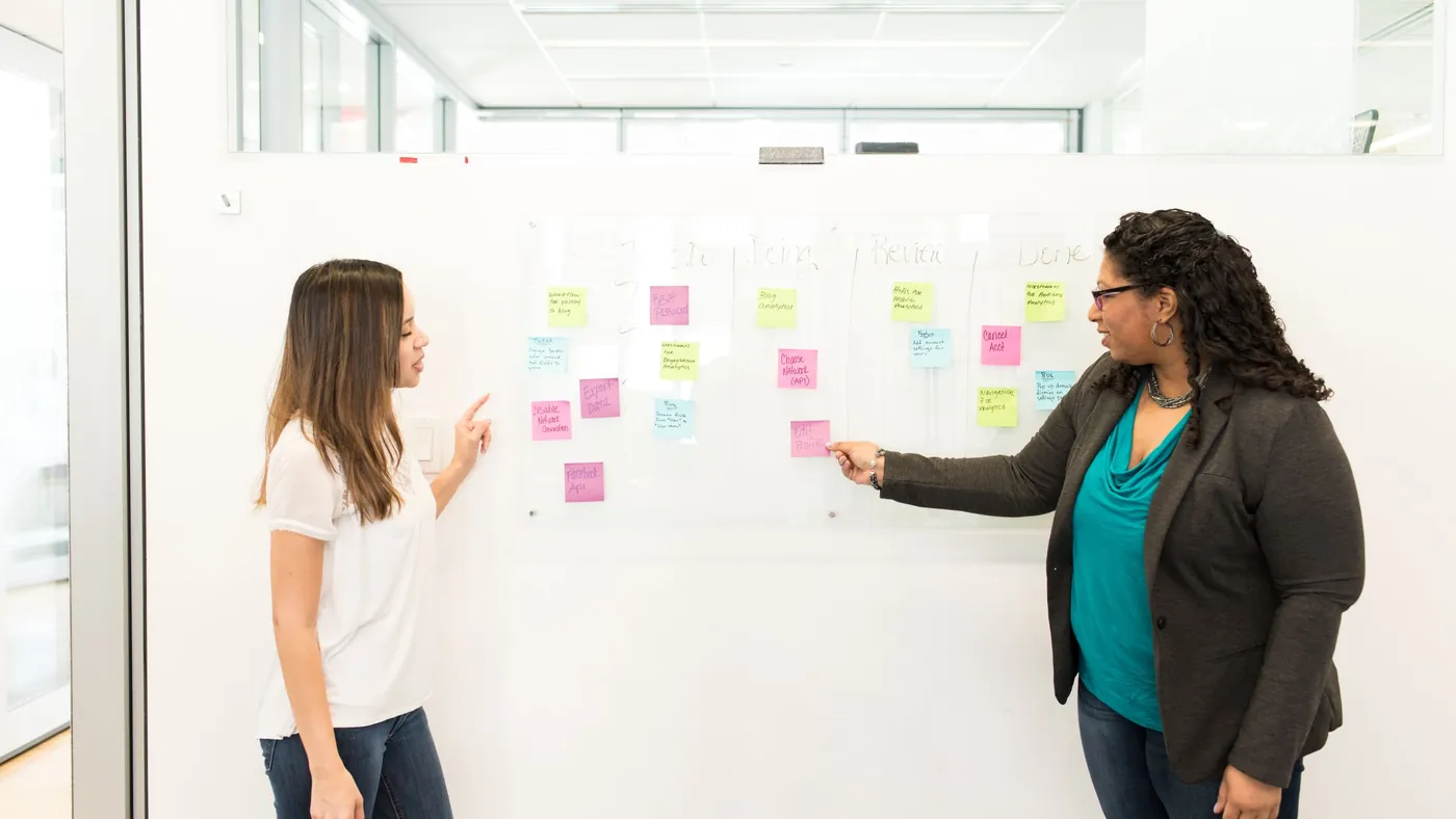 Two colleagues sorting sticky notes into groups on an office whiteboard