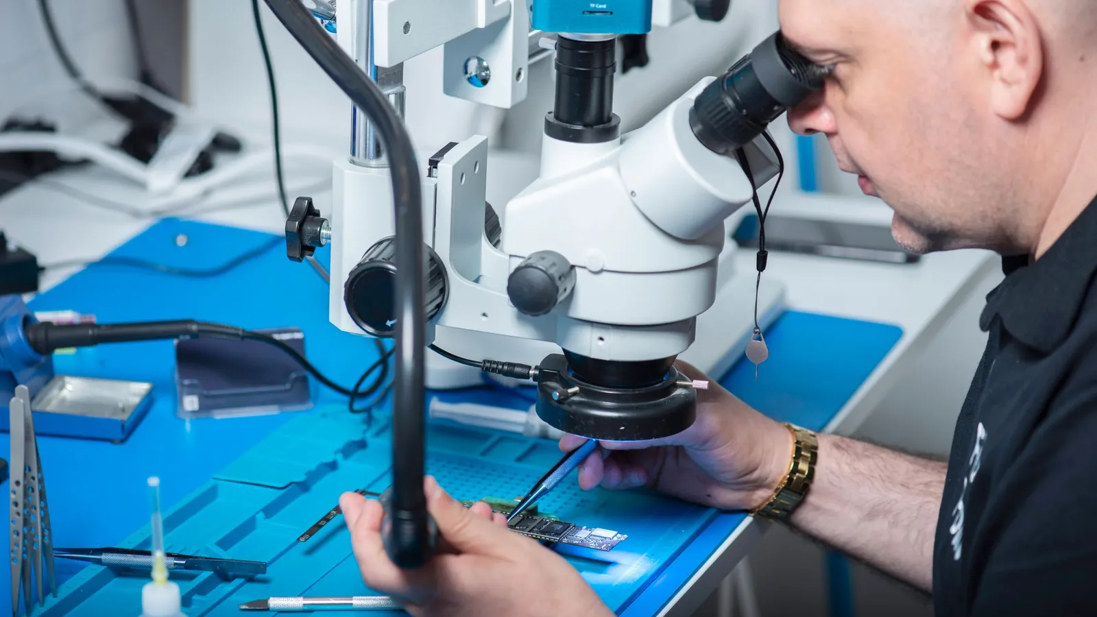 A technician looking through a microscope at an electronic component on a lab bench