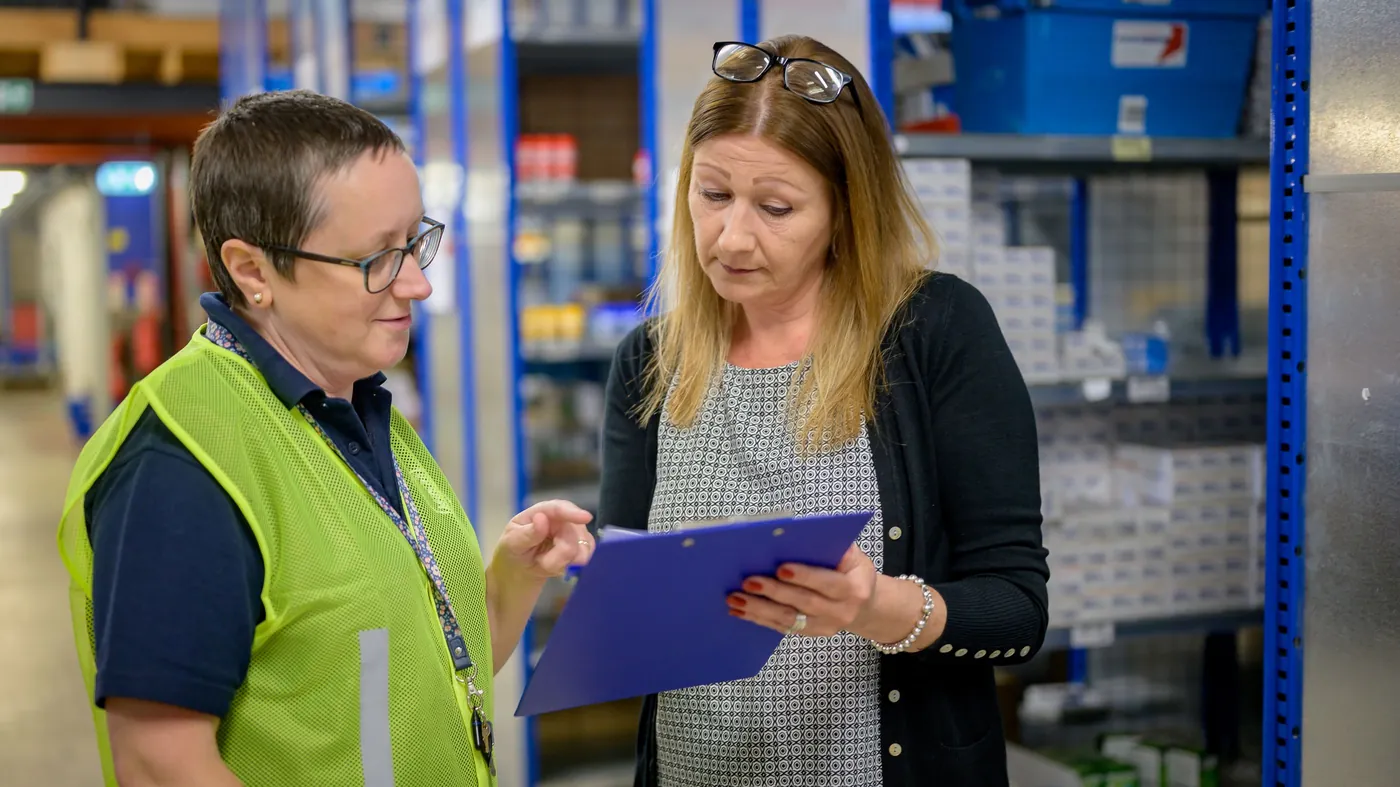 Two warehouse employees reviewing a clipboard checklist beside metal shelving