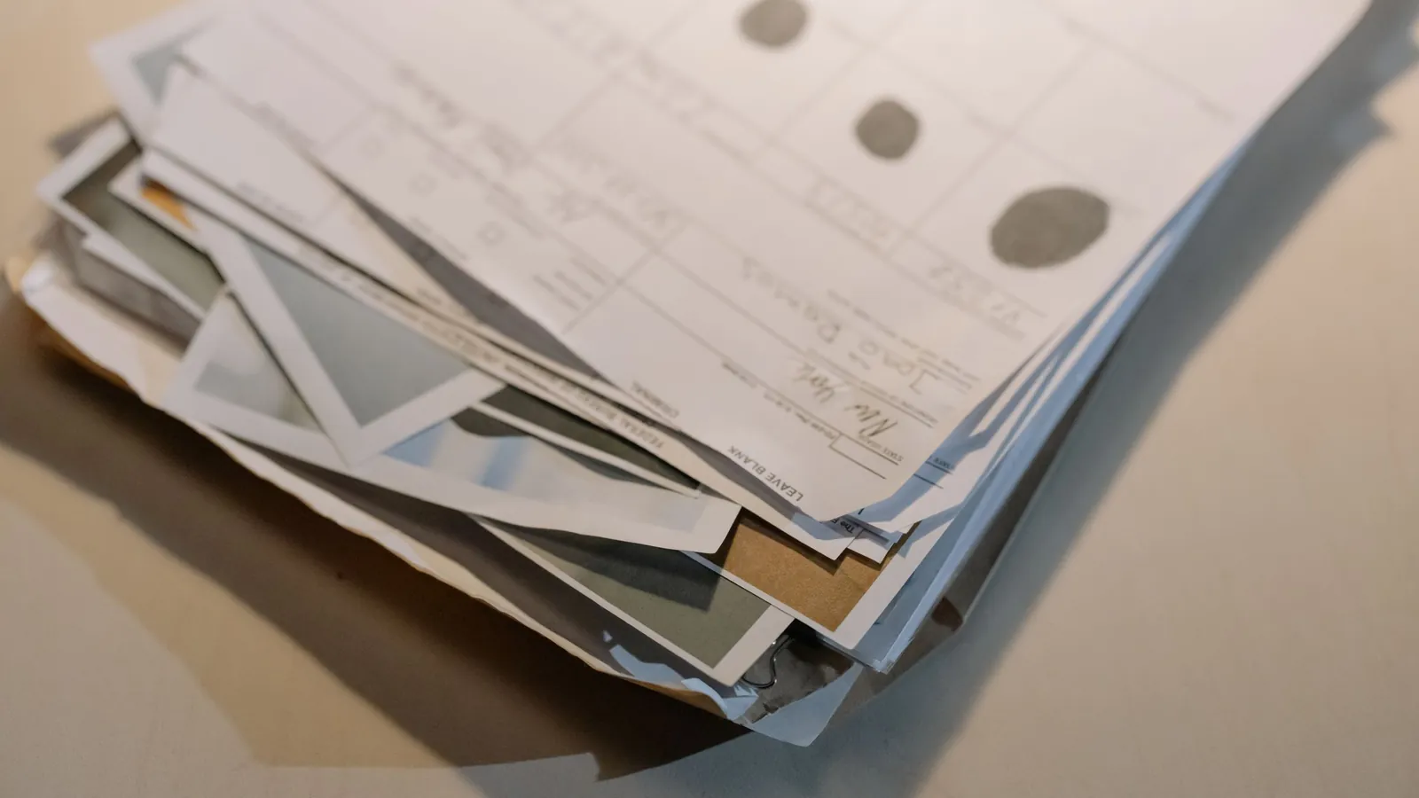 A thick, untidy stack of forms and photographs lying on a desk