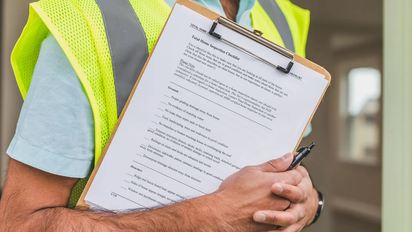 An inspector in a high-visibility vest holding a printed inspection checklist on a clipboard