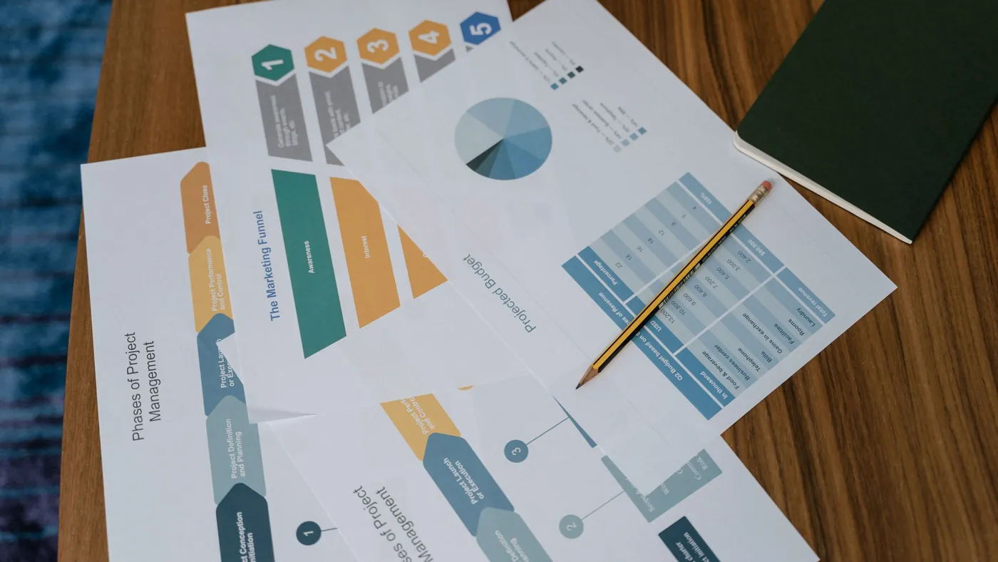 Overhead view of printed project documents and charts spread across a desk with a pencil