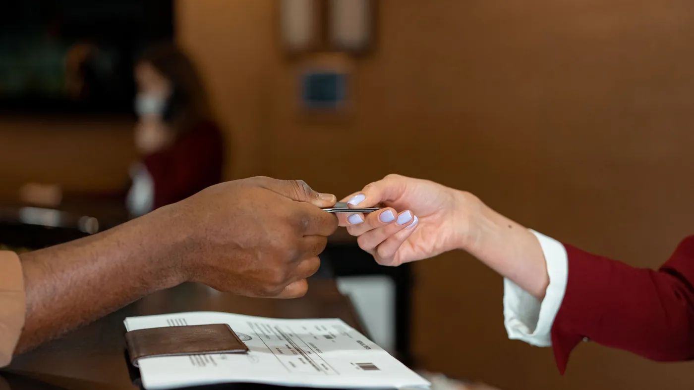 A guest handing a credit card to a hotel receptionist across a wooden desk