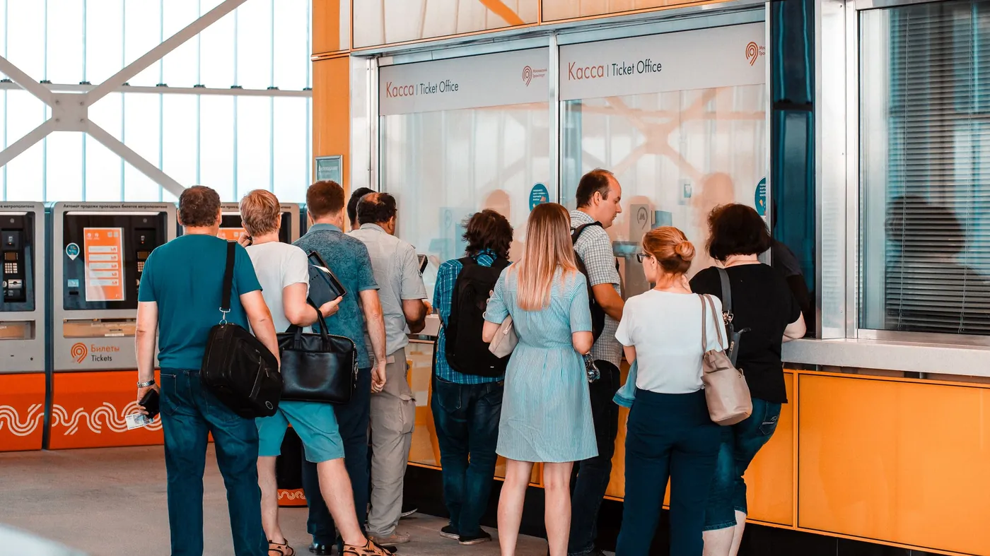 People standing in a single line at a ticket office counter, seen from behind